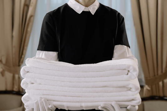 Hotel housekeeper in uniform holding a stack of neatly folded white towels
