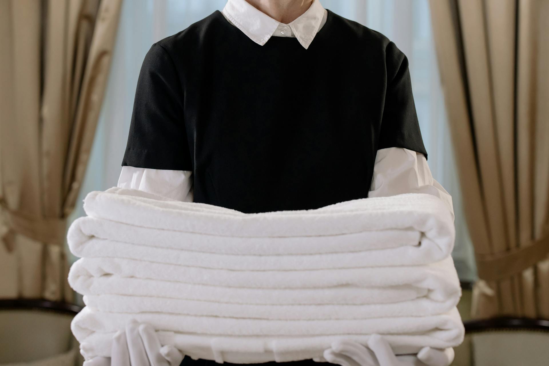 A housekeeper in a black uniform carrying a stack of white towels