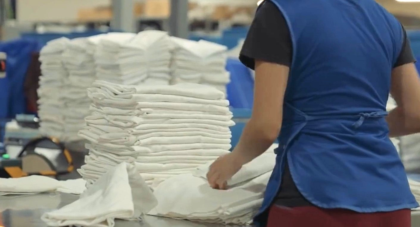 Worker folding white textile bundles in an industrial laundry facility.